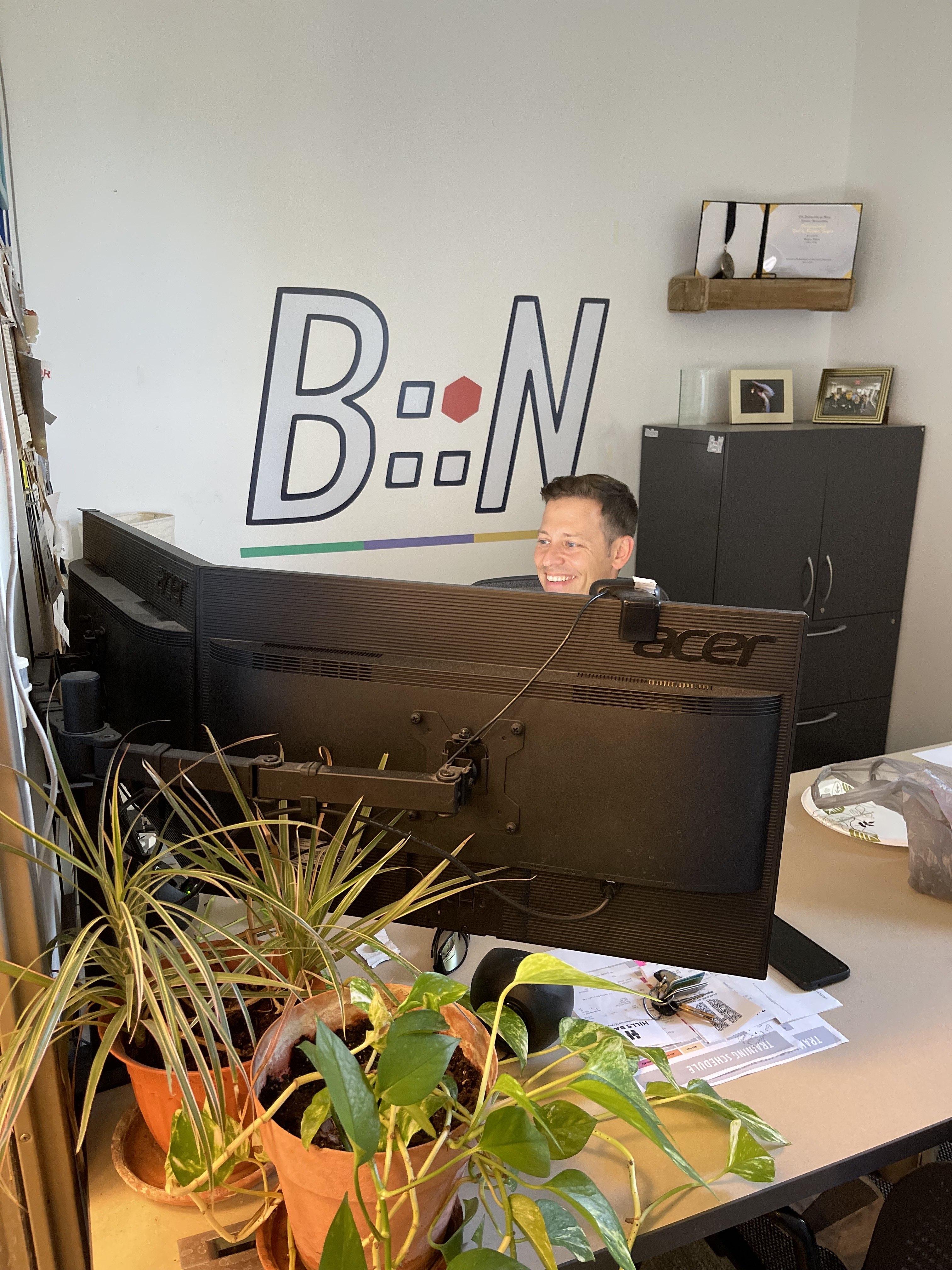 Steve working at his desk smiling with BN logo on the all behind him